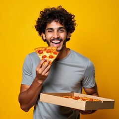 Young indian man eating delicious pizza on yellow isolated background. Happy handsome young teen boy holding slice of pizza