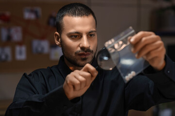 Male detective with magnifier examining evidence in office at night, closeup