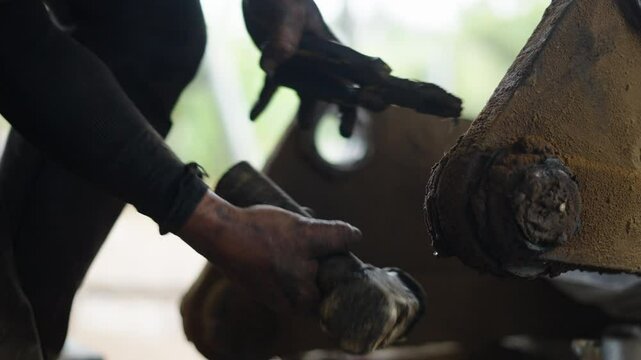 close-up hands of a mechanic removing the pin from an axle with a hammer and pliers