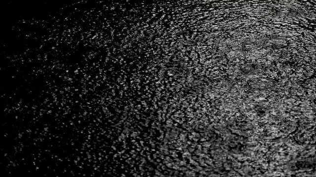 Tokyo, Japan -August 27, 2024: Heavy rain falling on a pool on asphalt pavement at night