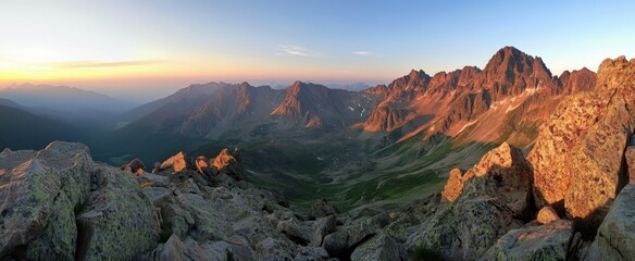 Panoramic view of the Tatra Mountains at sunset, showcasing rugged peaks, craggy cliffs, and dramatic rocky terrain.