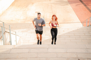 A sporty couple running up stairs to improve their leg muscles. Two athletic young friends doing cardio training on a stairway. Man and woman jogging doing a endurance workout outdoors with energy