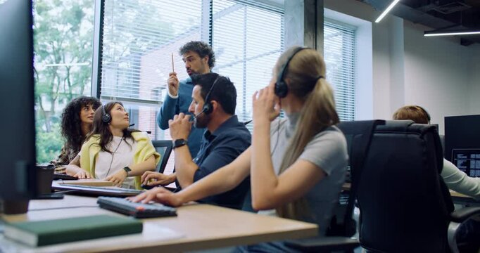 Smart manager distracting operators from work. Leader making announcements to colleagues while people sitting at their computers. Controlling quality of work. Sellers with headsets celling to clients.