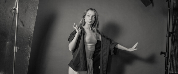 A young woman with a thoughtful expression posing in a studio, wearing casual attire, against a plain backdrop, captured in black and white, embodying contemplation and style.