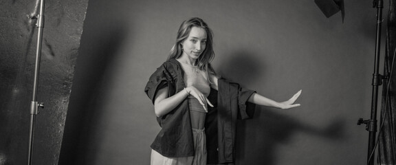 A woman is posing artistically in a monochrome photography studio setting, wearing casual clothing with dramatic lighting and shadows, creating a somber artistic feel.