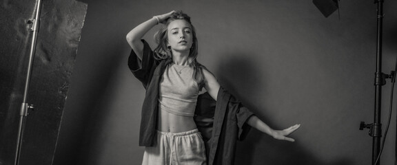 This black and white studio portrait captures a young woman elegantly posing in casual attire, highlighting expressive gesture and artistic lighting within a professional setting.