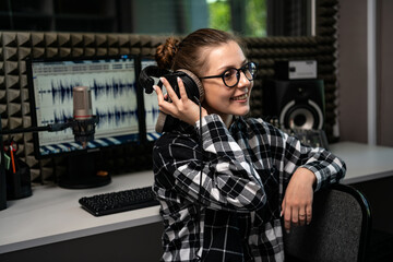 Portrait of cute female radio host with headphones and microphone in radio studio.