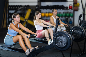 Young athletic woman training using rowing machine in gym