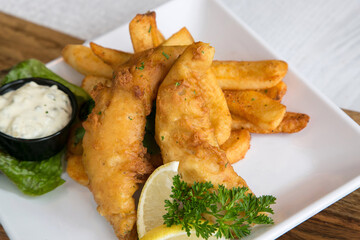 Fish and chips on white plate with tartar sauce and lemon wedge