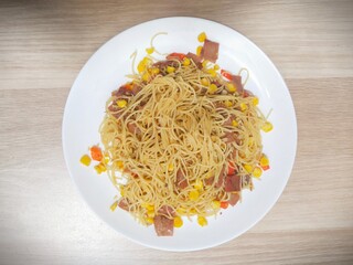 Homemade recipe classic aglio e olio pasta with smoked beef and corn, close-up in a white plate on the table