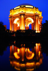 The Palace of Fine Arts in San Francisco is illuminated at night and reflected in the calm waters of the park