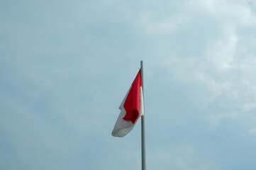 The Indonesian flag is red and white with an iron pole against a cloudy sky background.