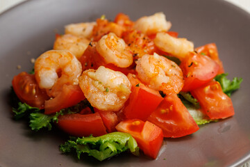 Fresh summer salad with shrimp, tomato and lettuce on grey plate close up. Concept of healthy eating