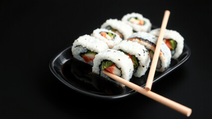 Close Up of Sushi Rolls with Chopsticks on Black Plate