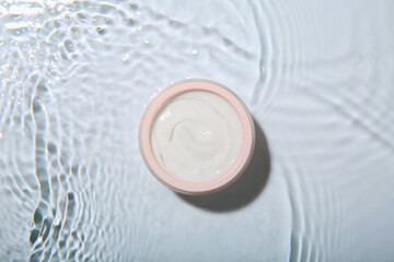 Cosmetic product. Jar with cream in water on light background, top view