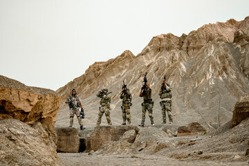 A group of military men in combat gear patrol in the middle of a desert and tropical jungle....