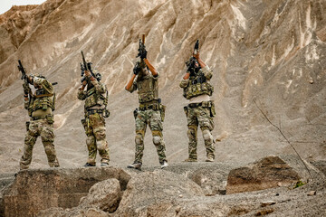 A group of military men in combat gear patrol in the middle of a desert and tropical jungle....