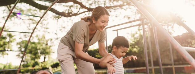 An Asian boy is having fun playing in a playground while his mother helps and ensures his safety. Active play and the joy of developing skills.