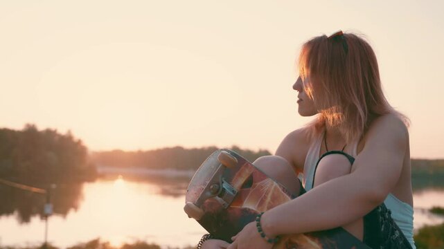 Dreamy Skater's Silhouette: Redhead Teen on Concrete Parapet | Side-Lit Slow Motion Portrait by Glowing River | Urban Sunset Scene with Board and Raised Sunglasses