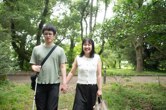視覚に障害のある白杖をついた男性が女性と手を繋いで散歩をしている