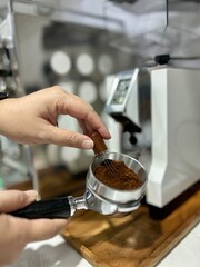 Closeup of hands of asian barista holding a portafilter declumping coffee grounds before preparing coffee with coffee grinder and espresso machine in the background