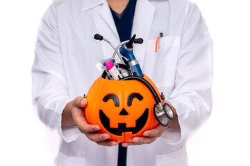 Unrecognizable doctor holding a Halloween pumpkin with medical instruments like a stethoscope, pills, thermometer, and otoscope; concept of medicine and Halloween, on a white background