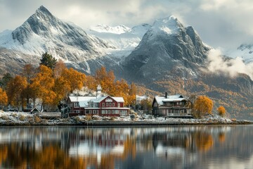 Fototapeta premium Two houses nestled amidst snowy mountains and fall foliage by a still lake