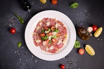 cooking tuna carpaccio - cherry tomato pieces on a plate with raw tuna fillet slices