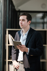 A man in a suit holding a tablet in front of a bookcase
