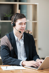 A man wearing a suit and a headset is typing on a laptop