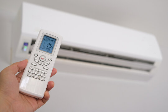 Man's hand using remote control open The air conditioner is cooled to 25 degrees Celsius in his bedroom. Health concepts and energy savings