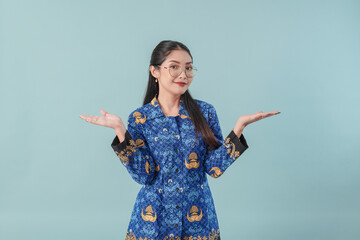 Confused government worker woman in blue batik uniform pointing to the copy space, choosing option.