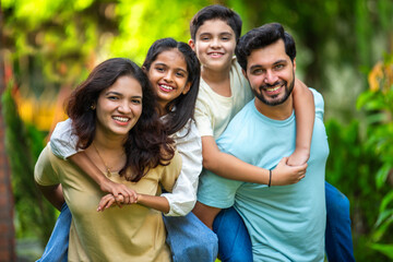 Happy Indian family enjoying playful piggyback rides with kids in a green park setting