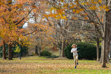Naklejka premium Funny kid running near autumn tree in the autumn park. Active child run and jump in autumn park outdoors. Little kid running near park. Autumn season.