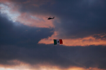 Ciudad de Mexico, Mexico - November 30. 2023: Helicopter in flight shows a Mexican Flag to people on the ground