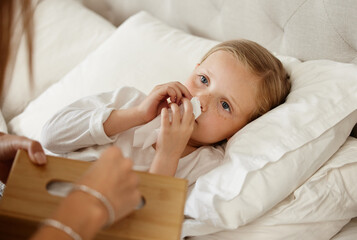 Sick, child and parent at bed in home for healthcare, wellness or tissue for cold treatment. Health, person and girl blowing nose for flu, virus or infection in bedroom with care, comfort and support