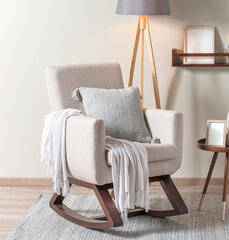 Scandinavian-style cozy nook with a modern rocking chair, gray pillow, fringed throw blanket, wooden floor lamp, and a sleek floating shelf in a tranquil, light-filled space.