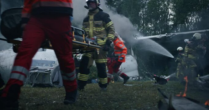 Plane Crash Site in the Forest: Firefighters Extinguishing Flames and Helping Paramedics to Carry Out Survivors on a Stretcher. Female Medic Assisting Young Man with His Wounds After the Wreckage