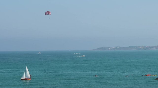 The beautiful Mediterranean setting at El Campello, Costa Blanca, Alicante, with a sailboat and individuals enjoying water sports like parasailing and boating.