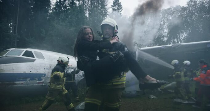 Firefighter Rescues a Female Plane Crash Victim, Carrying Her to Safety in His Arms. Firemen and Paramedics Extinguish Flames and Provide Medical Aid in an Emergency Scene