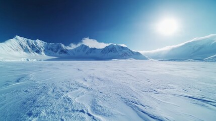 Fly over snow covered arctic winter landscape, towering mountains in background. Aerial view of frozen Antarctica panorama under blue sky in sunny day. Polar frozen ocean. Low angle aerial drone shot
