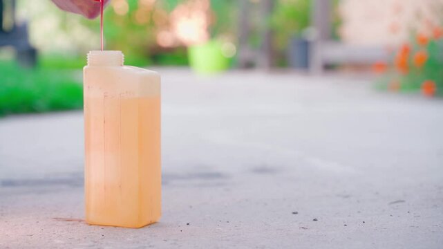 Pink gasoline lubricant is poured into the container for precise mixing of liquids. Preparation of gasoline for a two-stroke trimmer engine. Makes a gasoline-oil mixture
