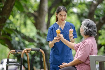 Elderly woman and young nurse enjoy ice cream together in a relaxing outdoor park environment