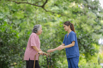 Elderly woman with walker receives caring support from young nurse in outdoor park setting.