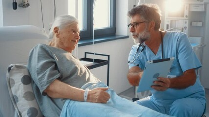 Elderly male doctor using digital tablet talking to senior woman patient at hospital, senior doctor showing results on tablet to old female patient in hospital ward