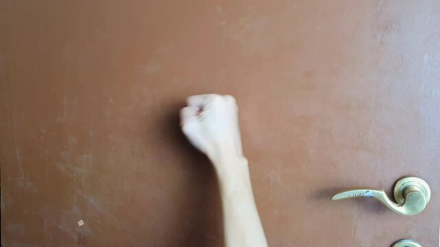 Closeup view of Someone is banging on a brown door with their right hand clenched into a fist, visitor standing in entrance, guest person wants to come in,free copy space, selective focus on fist hand