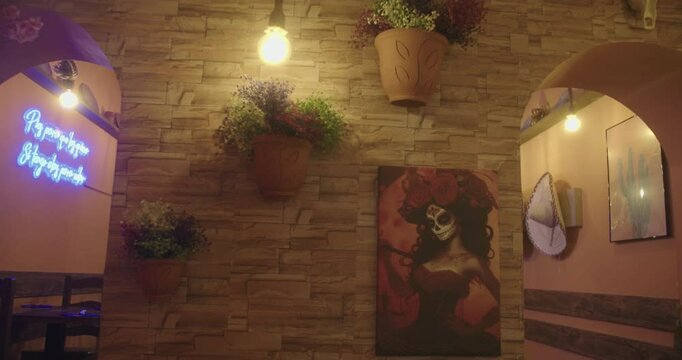 Beautiful general shot of an area of a Mexican restaurant with a decoration of potted plants, a picture of the holy death and low key lighting.