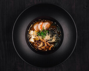 Steaming bowl of miso soup with tofu and shrimp on dark wooden table