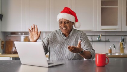 Happy senior man in santa hat making christmas video call on laptop in kitchen