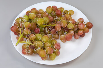 Clusters of pink grapes on dish on a gray background